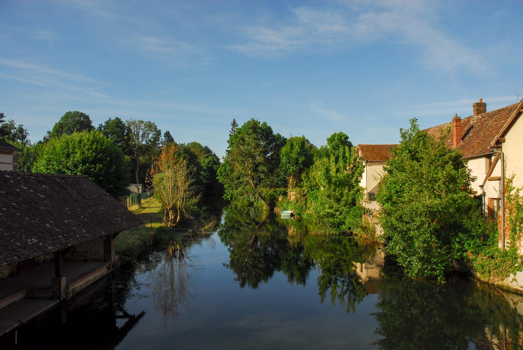View from the Bridge over river Eure. The water is completely still and mirrors the old houses and trees on the bank of the river.