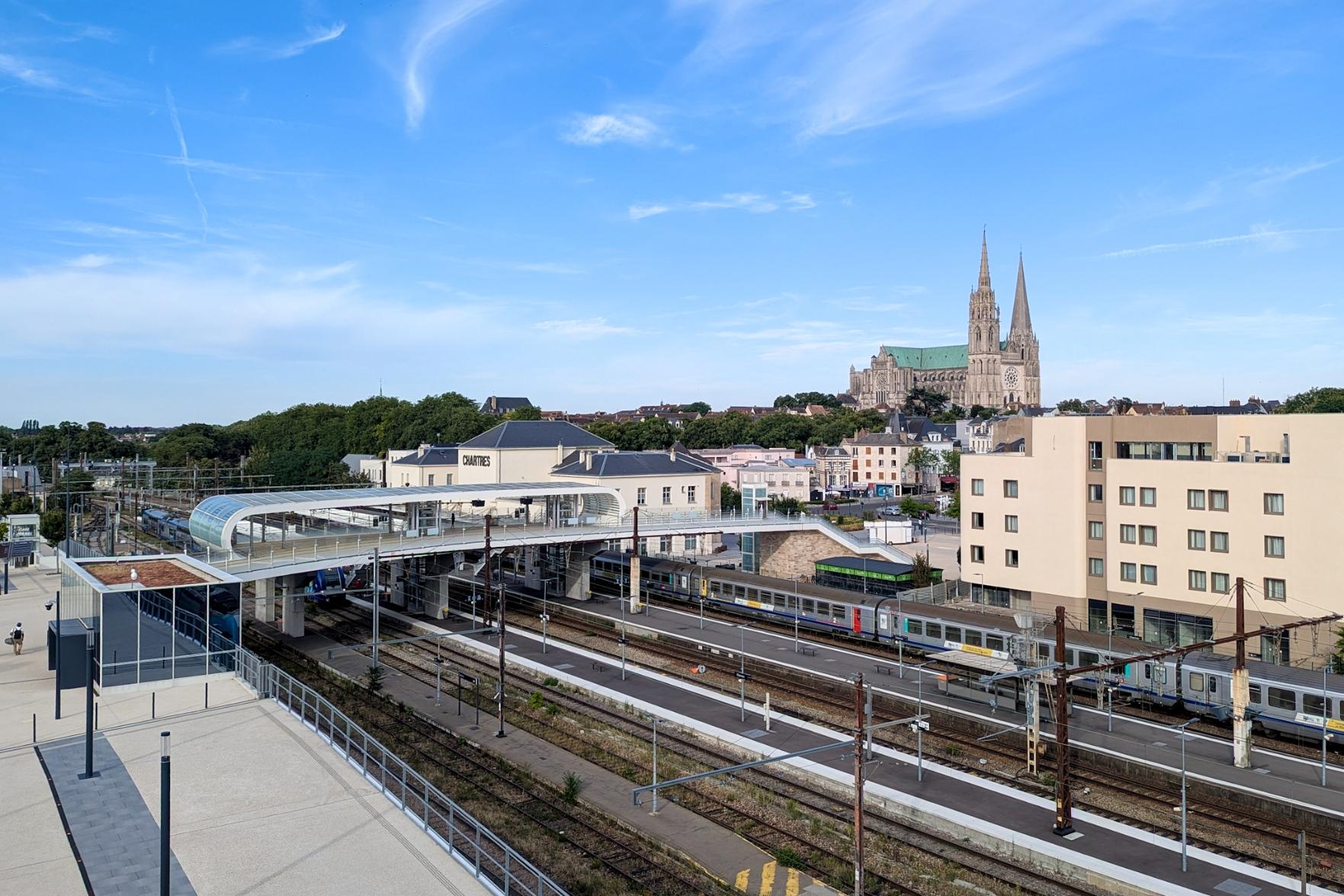 The new footbridge across the tracks at Chartres stations. Lifts and stairs leading down to the platforms. A Corail train on platform 1B, the Chartres cathedral in the background.