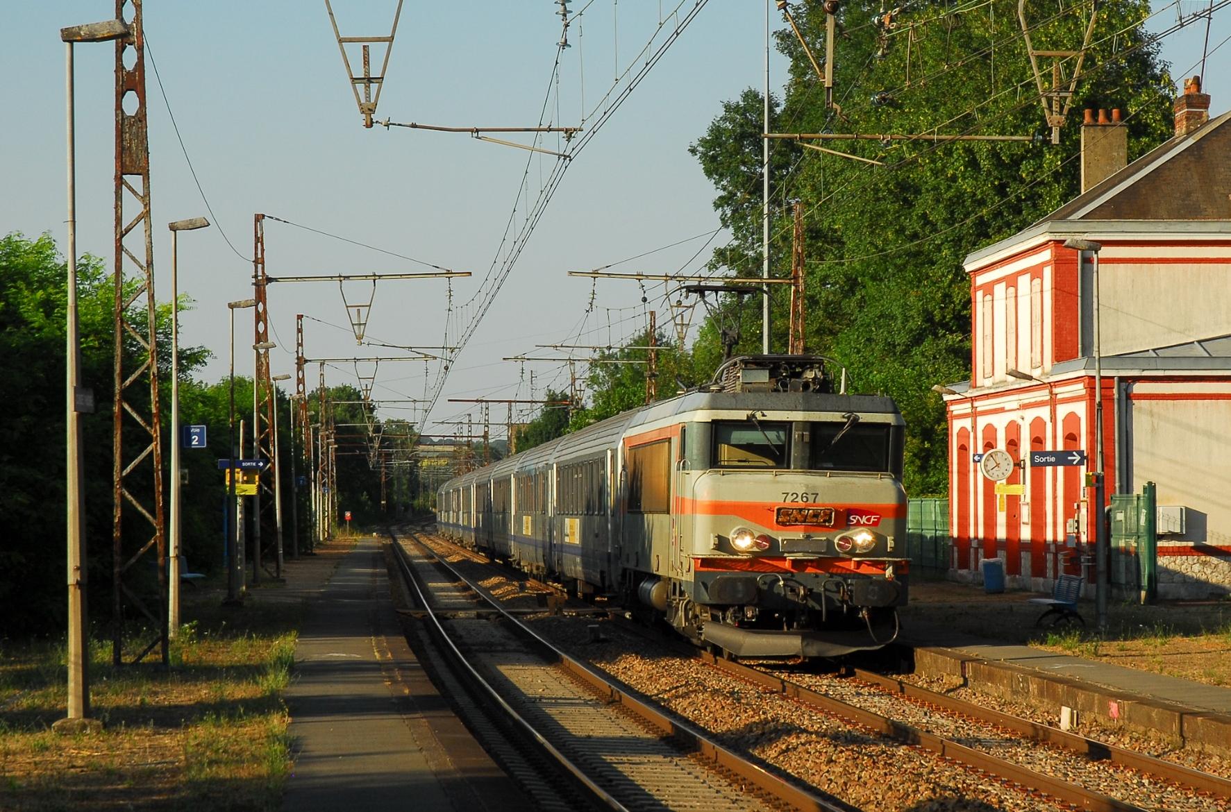 A béton liveried Nez Cassé BB 7200 with a long rake of Corail carriages bolts through the small station of Condé sure Huisne. An old, surprisingly big and surprisingly well preserved station building to the right - even if it's not in use anymore. Warm evening light, the bushes on the platform throw long shadows on the train.