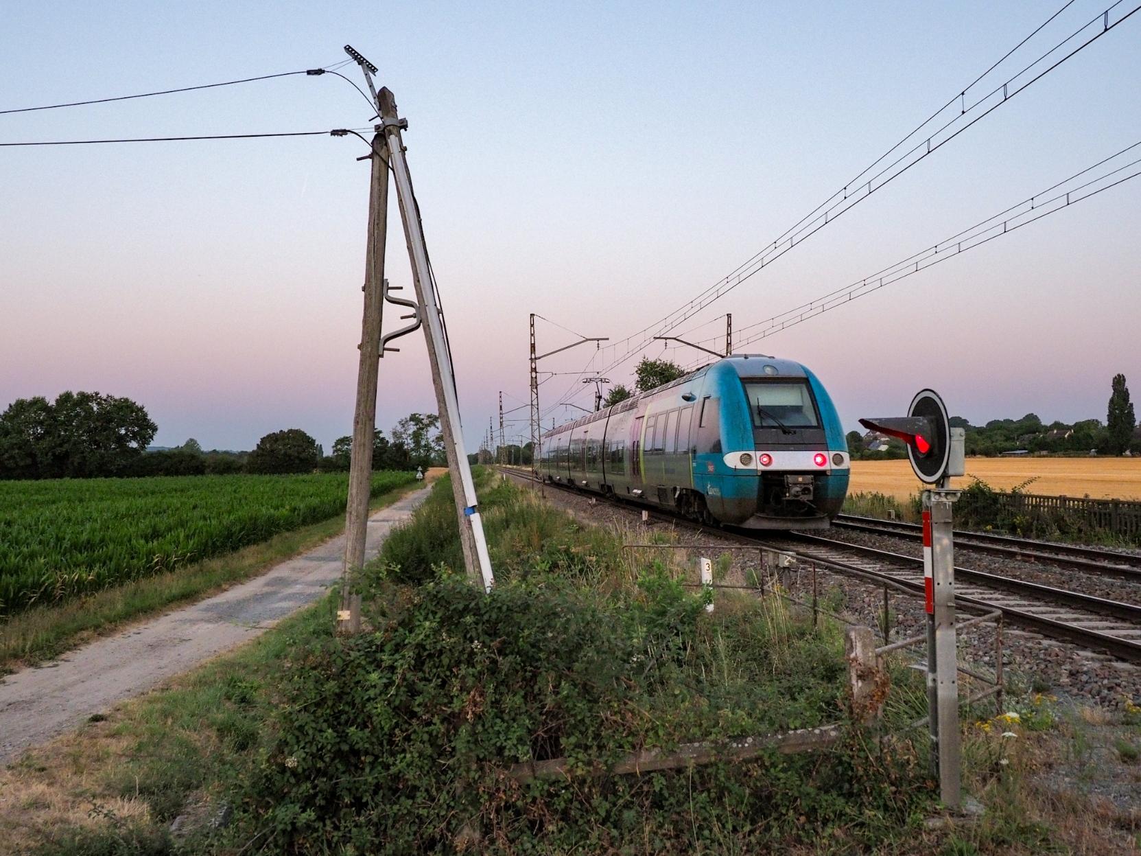 In a strange grey light shortly before sunrise, an AGC passes. Straight stretch of line across fields, old catenary, a wooden electricity or telephone pole to the left.