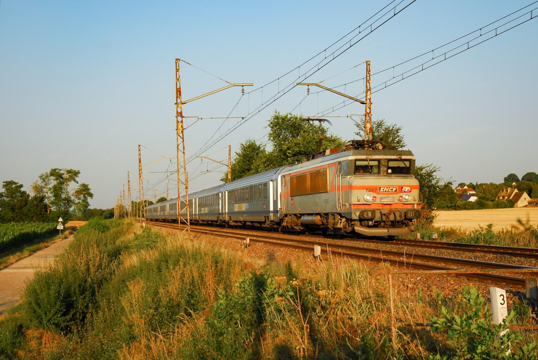A Néz Cassé in livrée béton hauls a rake of Corail carriages under old, rusty askew catenary masts.