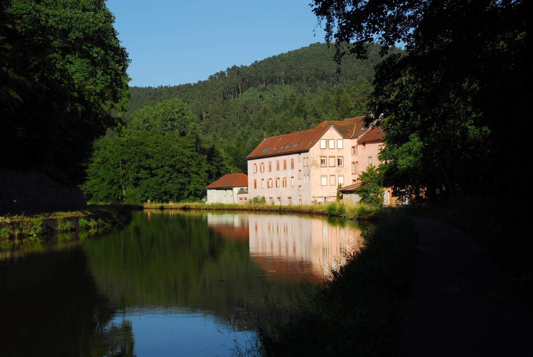 An old multi-storey industrial building at a canal in the forest in the warm evening light.
