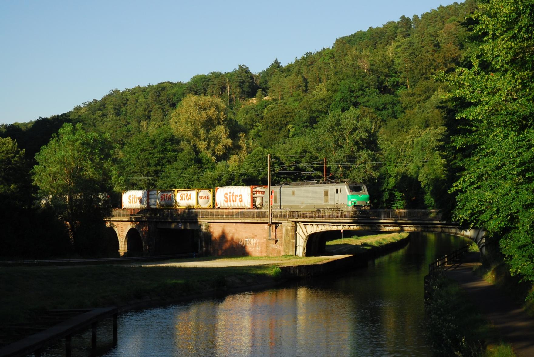 The same spot as before, only that the shadows have advanced considerably towards the bridge. A Prima locomotive hauls a container train towards the West.