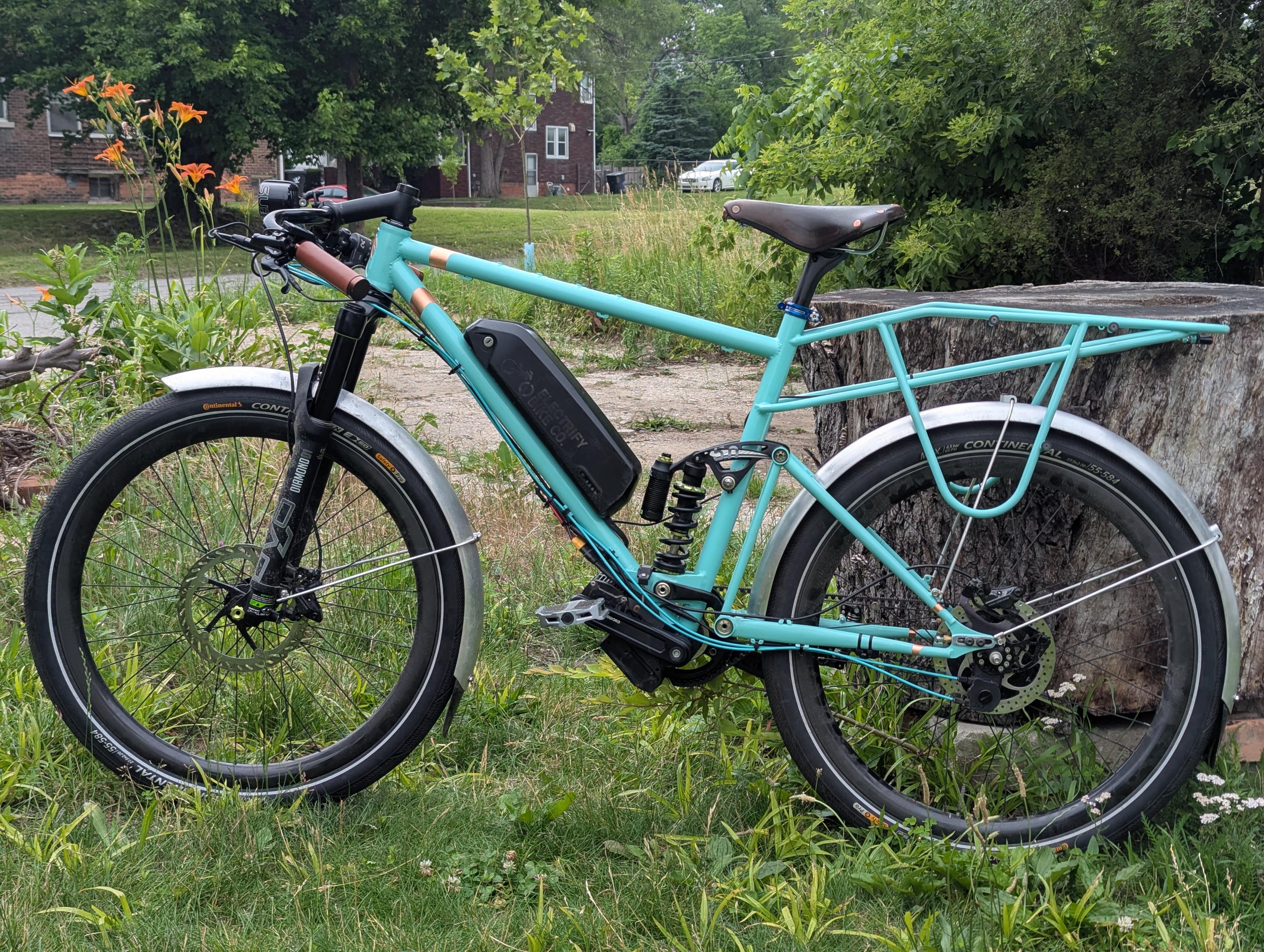 A teal commuter bicycle, full suspension with aluminum fenders and a rack attached to the main triangle