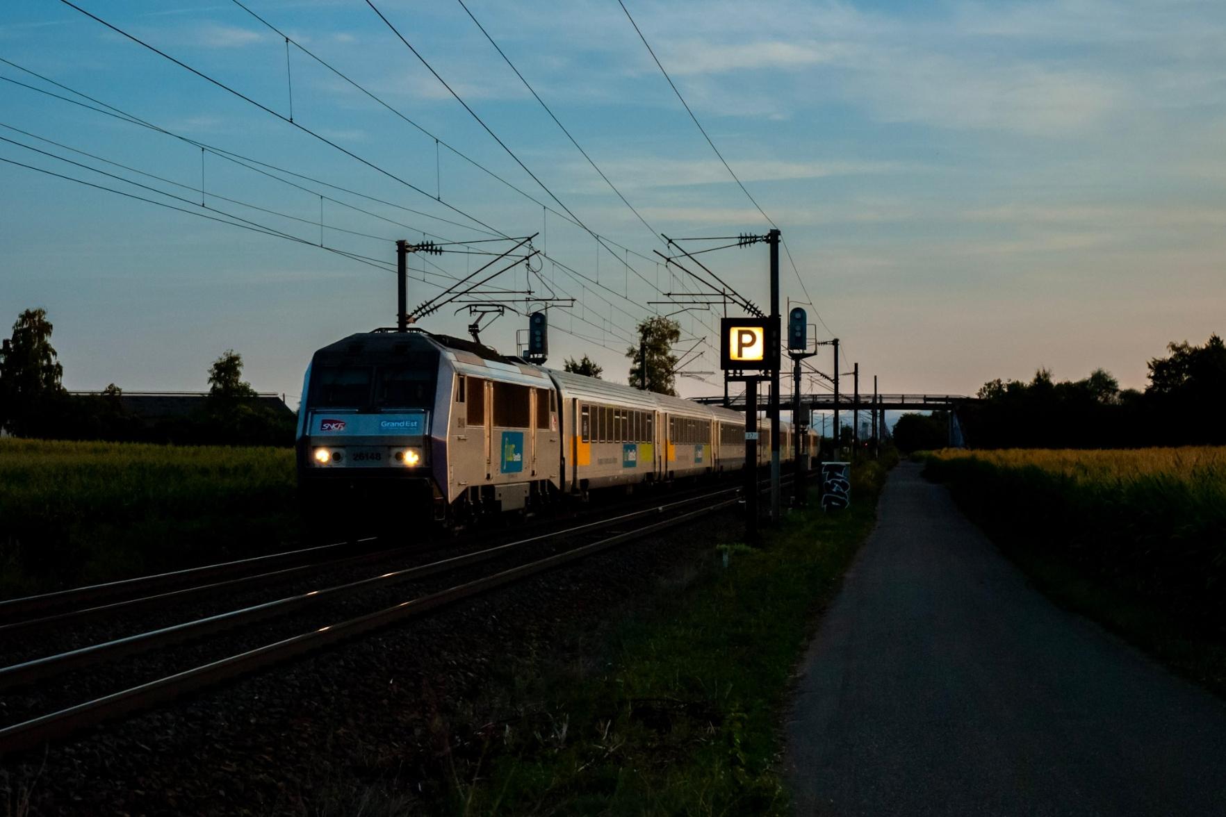 A Sybic loco with a Corail rake. The sun has set, but the last light of the day reflects on the side of a train. A backlit P signal for the opposite track.
