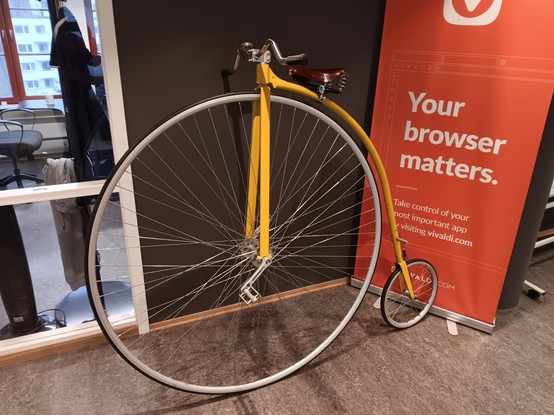 A bright yellow penny farthing ("ordinary bicycle") inside a building next to a sign that says, "Your browser matters" and the Vivaldi browser logo.