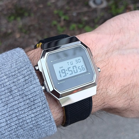 Steel LCD digital watch in Casio style with a black strap that is yellow underneath. 