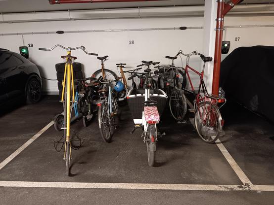 A bunch of different types of cycles in a car parking spot in a garage. 
