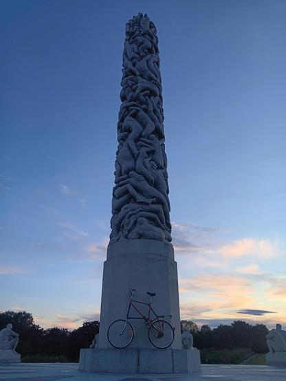 A tallbike leaning against the Monolith in Oslo's Vigeland Park, in the evening. 