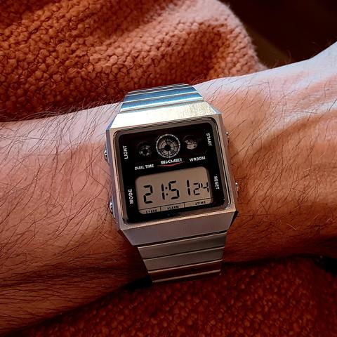 Skmei digital watch, square in shape. Above the main dial are two animated LCD spinners and a tiny LCD map. 