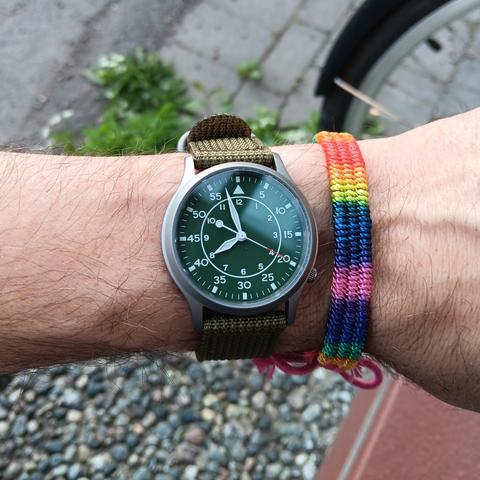 Green flieger type b dial with a green background. On the wrist is a cotton rainbow band. 