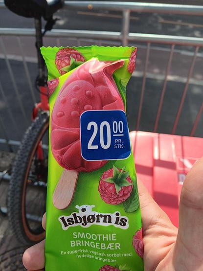 A hand holding a raspberry smoothie ice cream. In the background you can just make out a unicycle