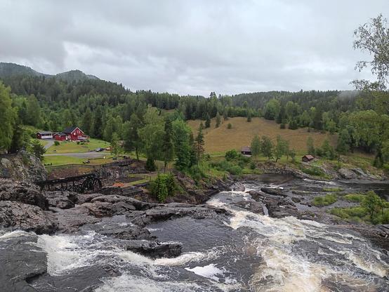 Picturesque view of a river and waterfall with old farm buildings. 