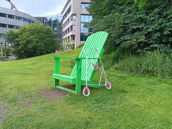 A tallbike with tiny wheels, next to a very if chair. 