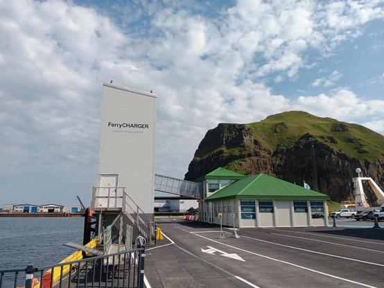 Picture of an electric ferry charging station. In the background is a massive Rocky outcrop jutting out of the water. 