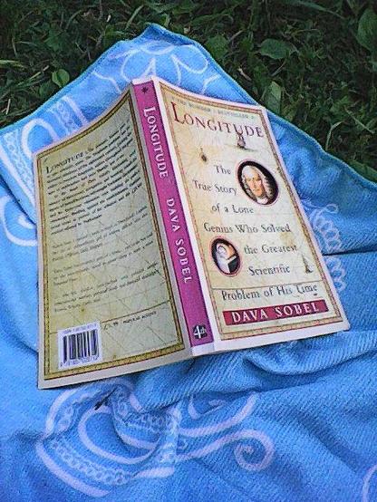 A picture of the book Longitude by Dava Sobel. Opened and resting on a beach towel. 