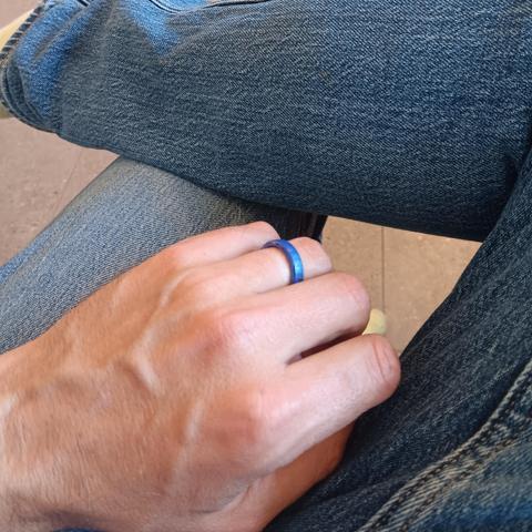 Mans hand resting on blue jeans, wearing a blue ring. 