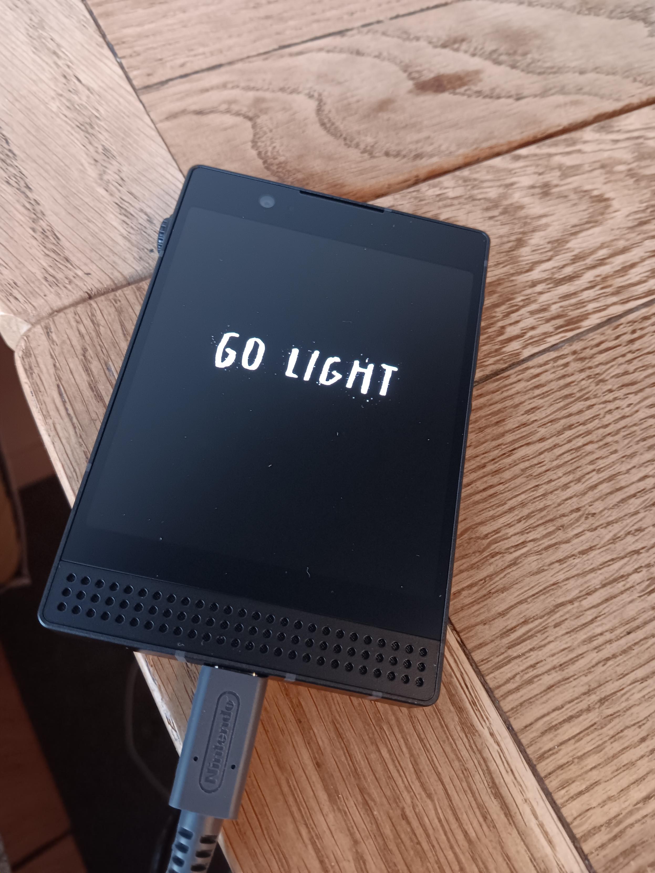 Lightphone III on a wooden desk showing the stylised text, "Go light"
