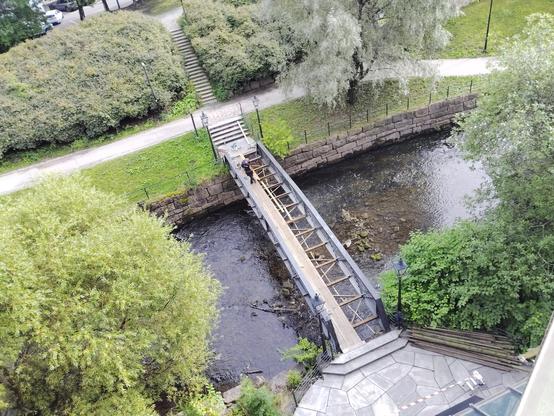 View from above looking at a footbridge. Much of the walking area is removed and there are two workmen on it.