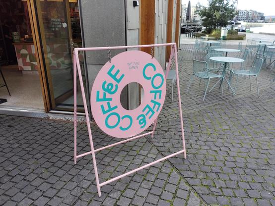 I donut shaped sign that says coffee in teal on a pink background
