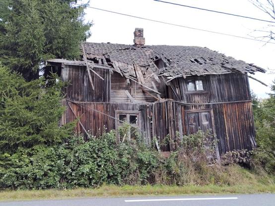 An old wooden house that is slowly decraying and has lots of trees and bushes around it.