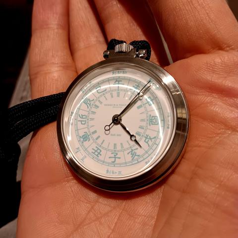 Pocket watch in the palm of my hand. It has a 24 hour movement showing the time with Roman Numerals and also Shíchen (时辰). An old Chinese timekeeping system that divides the day into 12 two-hour periods, each represented by a zodiac animal. The time shown is 21.07. 