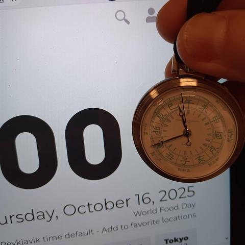 A pocket watch helf in front of a computer monitor. On screen you can see 00 (representing seconds), while on the pocket watch the second hand is two seconds away from the start of a new minute.