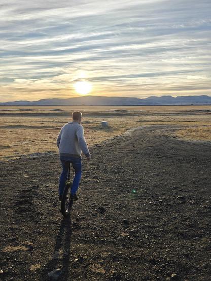 A man unicycling towards the sunrise along a gravel path. 