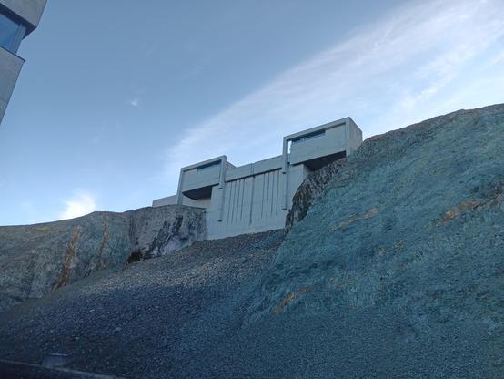 A concrete building with a very brutalist design, surrounded by rocks. Looks like it could be from Star Wars.