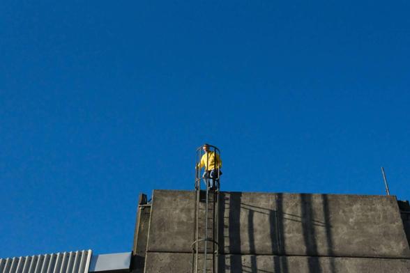 Man with yellow jacket on an industrial looking building. Very blue sky. 