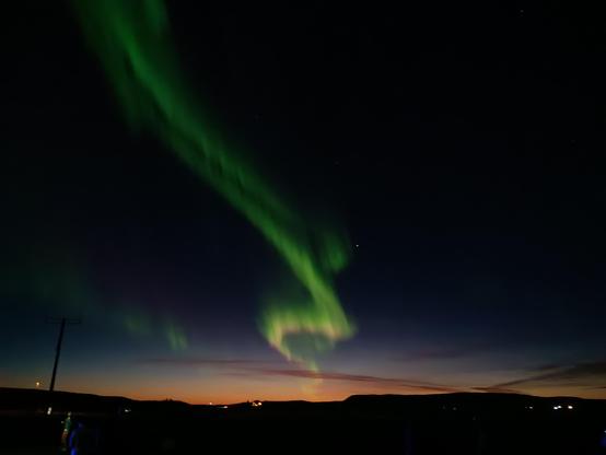 Green and a little pink in the night sky above dark hills. 
