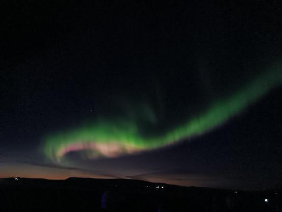 A swirl of pink and green across the entire sky abivevvery dark distant hills. 