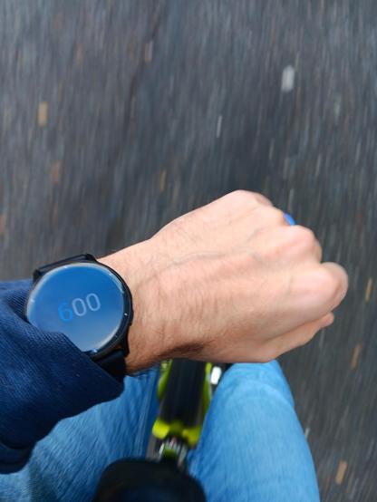 A green unicycle from the rider's perspective. They are wearing a watch that shows the time 6.00.