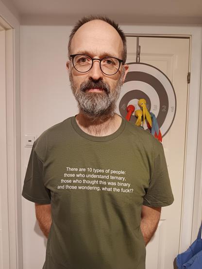 Middle aged whit man looking at the camera. He is wearing a green T-shirt that has the following written on it:

There are 10 types of people: those who understand ternary, those who thought this was binary and those wondering, what the fuck!?