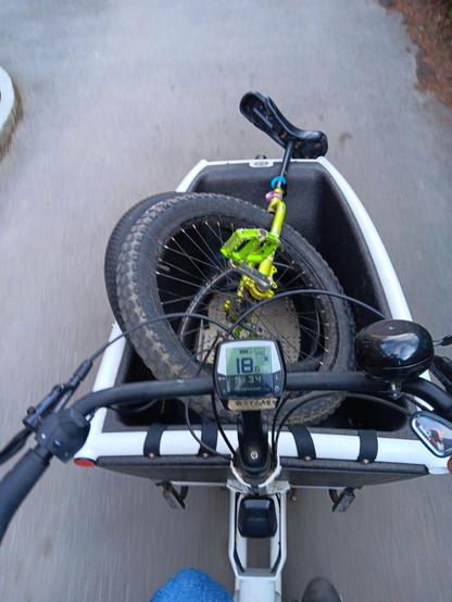 Looking down at a cargo bike from the rider's perspective. Inside the cargo area is a unicycle.