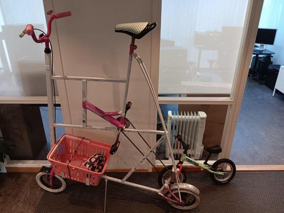 A very tall pink and white bike with tiny wheels and a pink basket, alongside a small green balance bike.