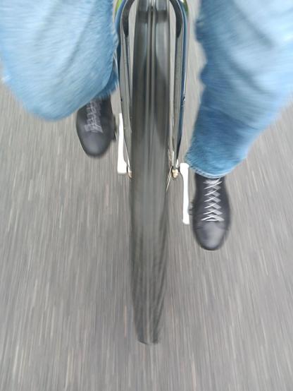 View from the rider of a unicycle, looking down at a very large wheel. The shoes of the rider have their laces tucked neatly in.