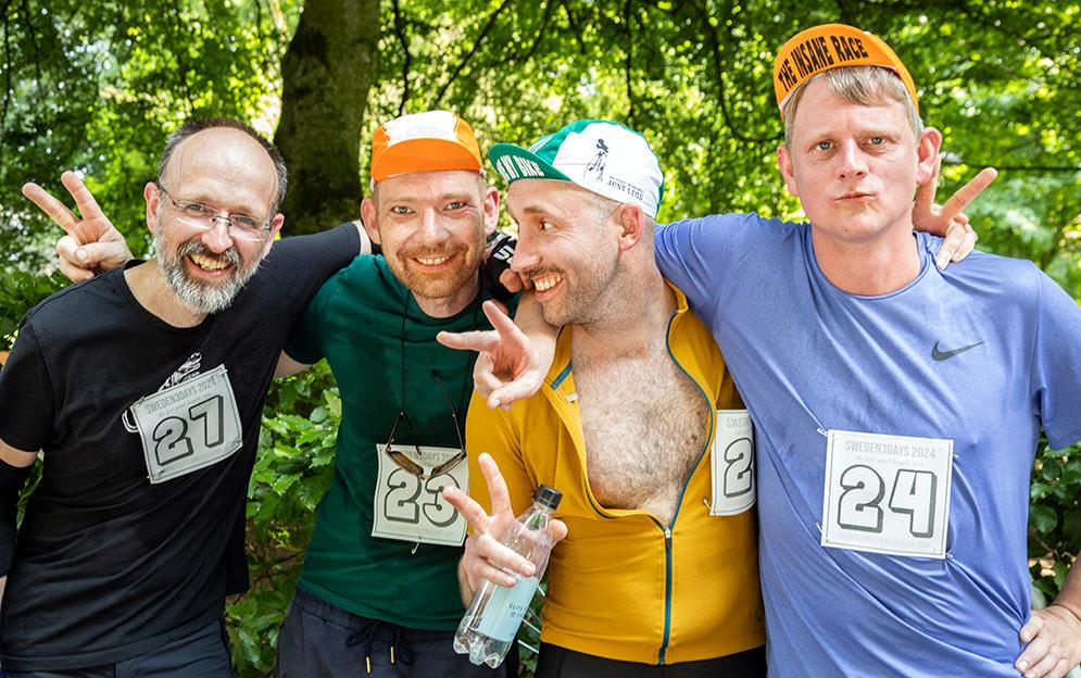 Four mean smiling in cycle racing gear. The middle one is looking to one side and has his nipple out.