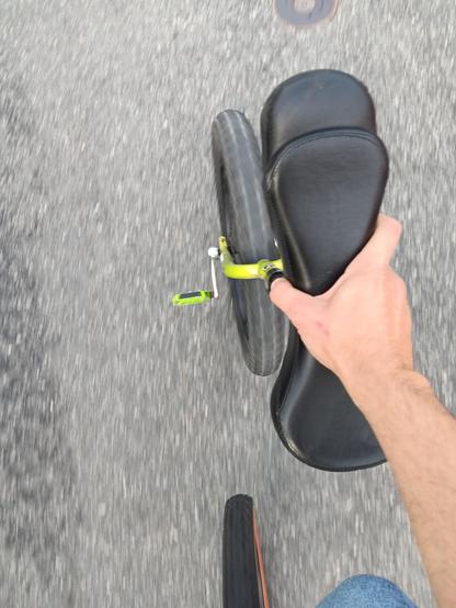 Looking down at a hand holding the seat of  unicycle. There is also another wheel at the bottom of the photo. 