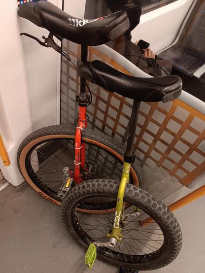 A red and green unicycle leaning against the glass partition on transit.