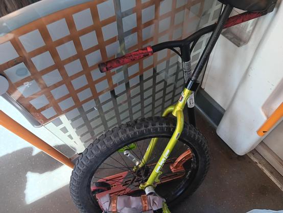 A green unicycle leaning on an orange kick scooter, with a backpack on public transit. 