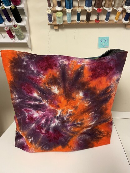 Unobstructed view of the orange, purple, raspberry swirl side of the tote bag. 