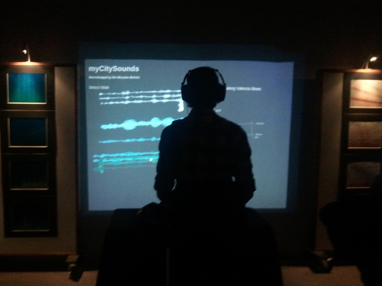 Photo of a tall man wearing headphones and interacting with an installation of myCitySounds which is projected in front of him.