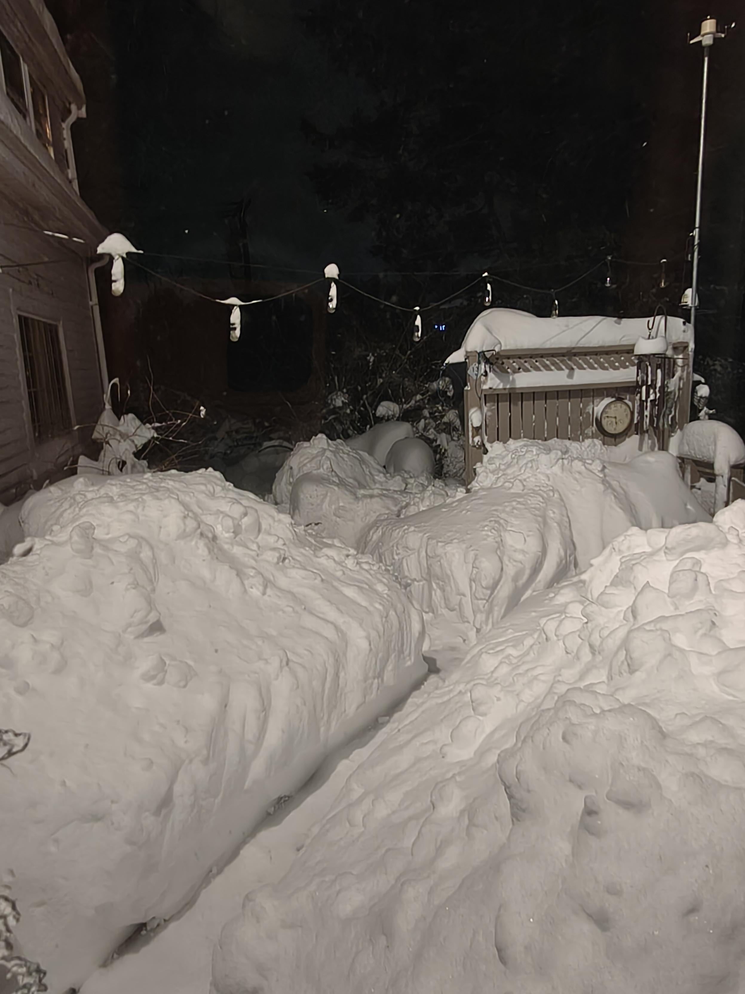 A five-foot deep canyon of snow across a wooden deck. The actual snowfall was less (maybe 30"?) but with drifts and shoveling a pathway, the piles have built up ominously on either side in this nighttime view. A few snowflakes can still be seen falling again the inky black sky.