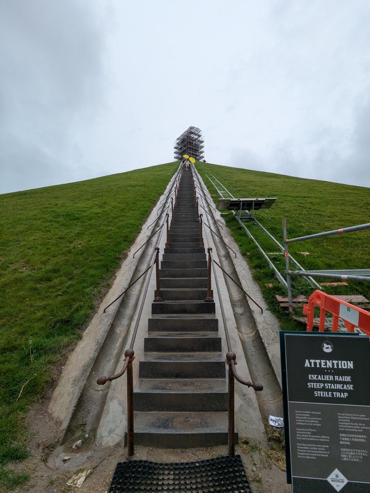 Steep stairs running up to the mound of the lion (Butte De Lion) on the historic battle site of Waterloo in Belgium.  The mound is covered in grass, at the top there is a lion statue, but it covered in scaffolding.