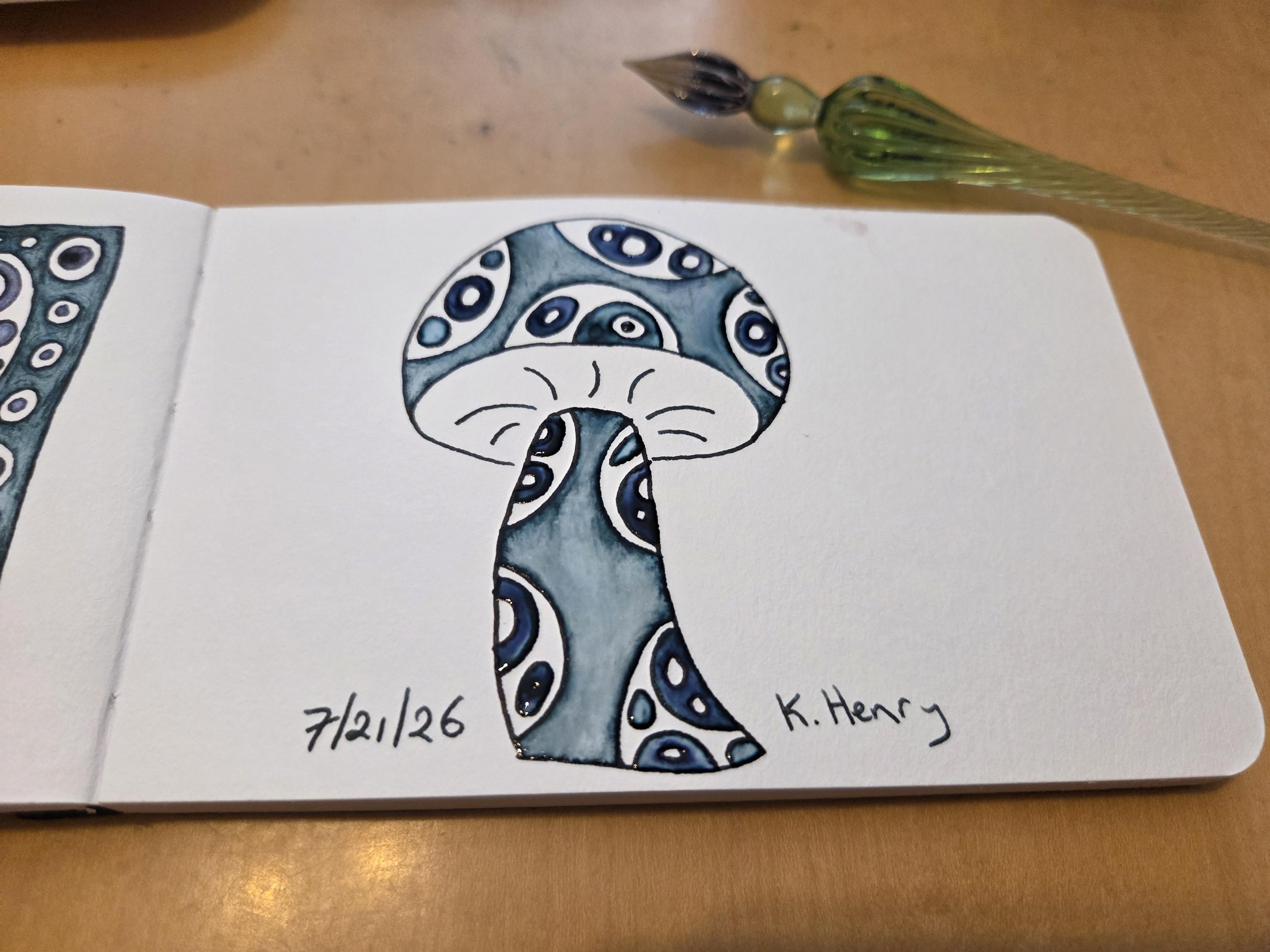 Hand drawn generative/procedural art in ink on an open page of my sketchbook. The abstract pattern looks a bit like a mushroom with spots on the stem and cap. My glass dipping pen is next to my sketchbook.