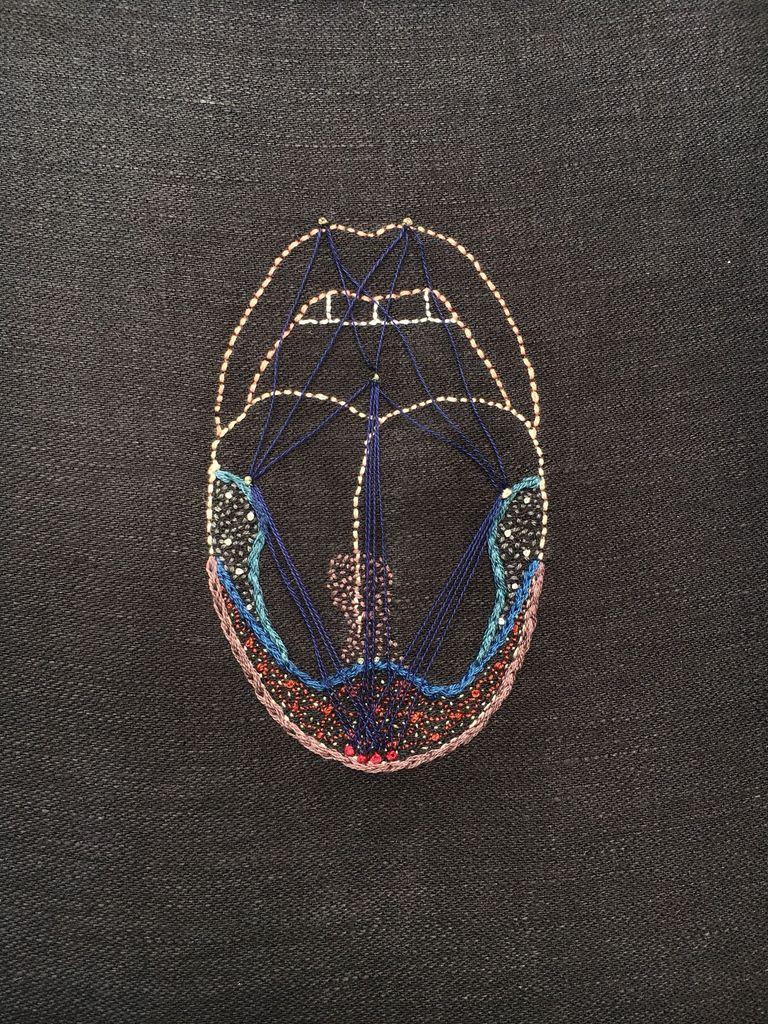 Paresthesia (tongue 2) 2018. An embroidery on black linen. There is the outline of an open mouth with the tongue sticking out. The lips are outlined in dark pink, the tongue in paler pink, & the teeth in bone white. There are sections outlined on the tongue in thick blue lines. The tip & sides of the tongue are covered in tiny red, orange & white dots. In the center there is an hourglass shape of tiny pink dots. There are taut lines of thin dark blue thread stretched from the tip of the tongue to the sides, from the sides of the tongue to the lips & palate, & from the palate to the tip of the tongue.