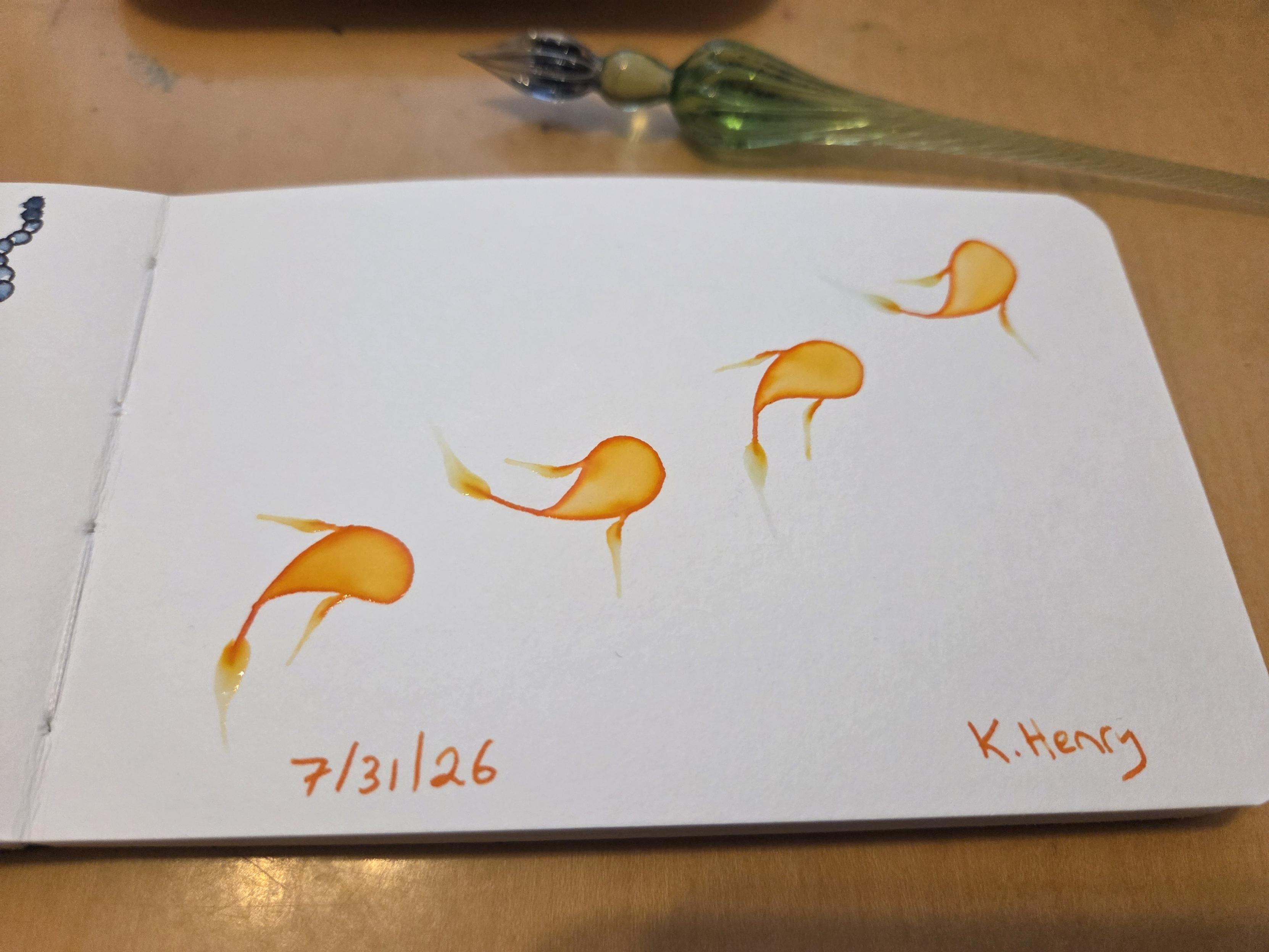 Hand drawn generative/procedural art in ink on an open page of my sketchbook. The abstract pattern looks like four little fish swimming in a line across the page. My glass dipping pen is next to my sketchbook.