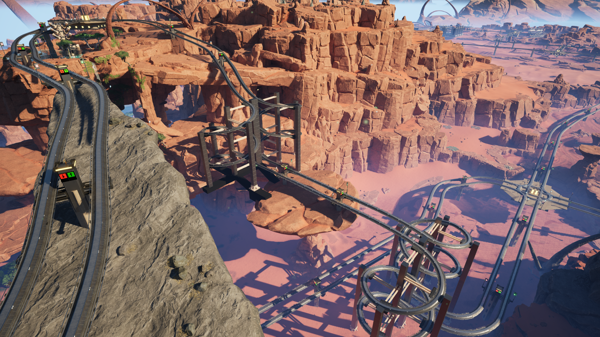 Satisfactory video game screenshot: A rocky promontory, some red cliffs, and a canyon floor, all with train lines running over, around, and through. Spiraling structures are used at two locations to achieve most of the elevation change.