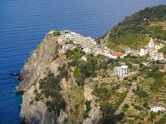 Vue aérienne du village de Corniglia en Italie, perché au sommet d’une falaise escarpée avec des champs en terrasses descendant vers le littoral.